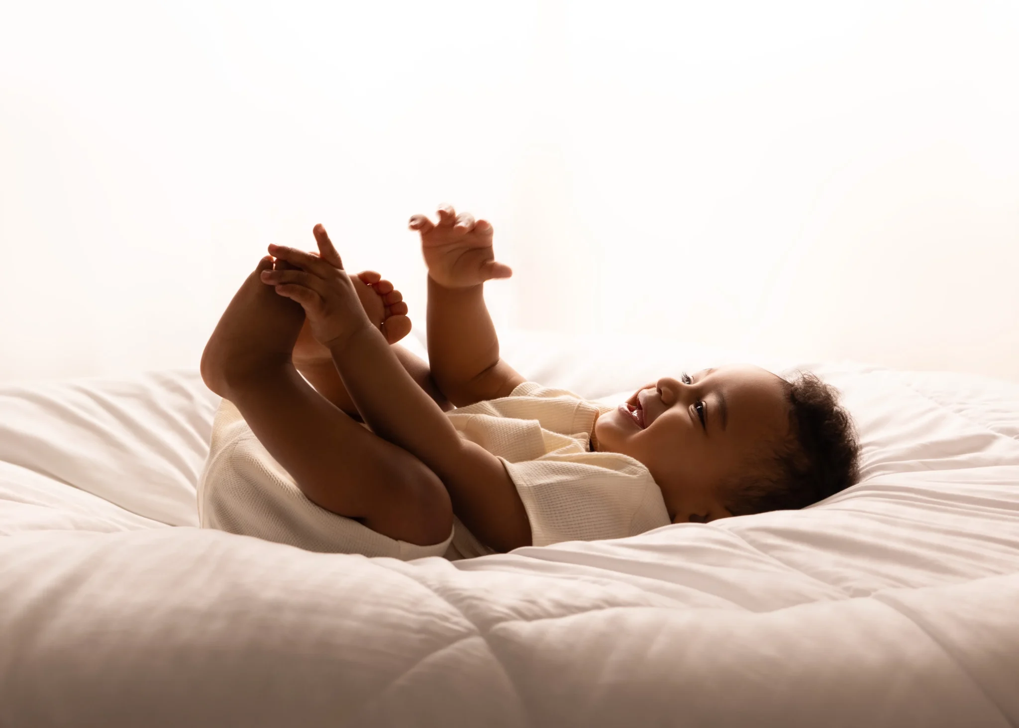 Backlit baby laughing on a white bed at Soul Studio, Amman