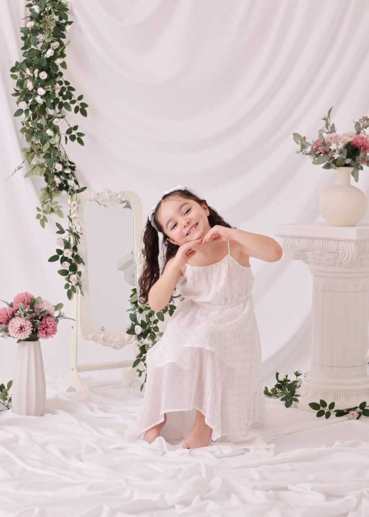 Little girl in a white dress among flowers and mirrors at Soul Studio
