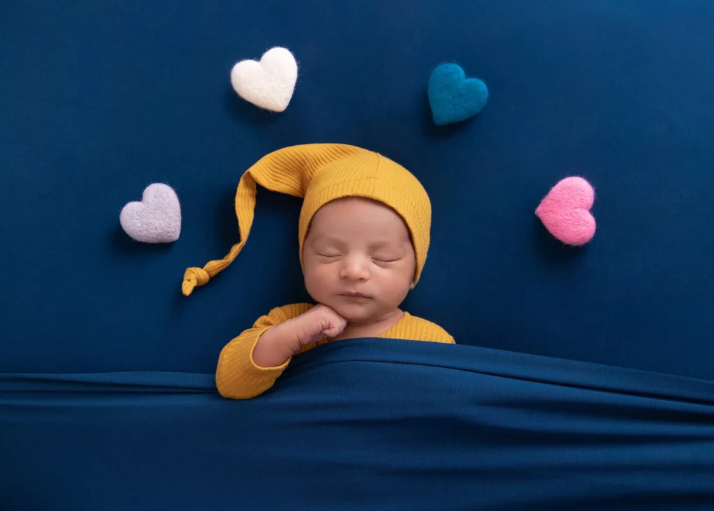 Newborn in a yellow cap sleeping among soft felt hearts at Soul Studio